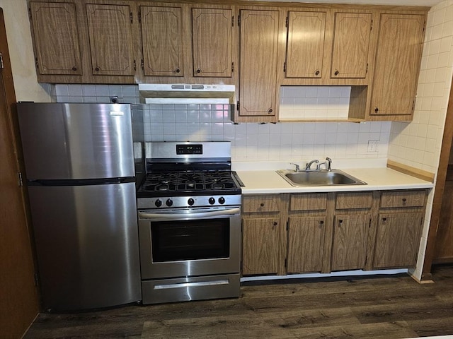 kitchen featuring light countertops, under cabinet range hood, a sink, backsplash, and stainless steel appliances