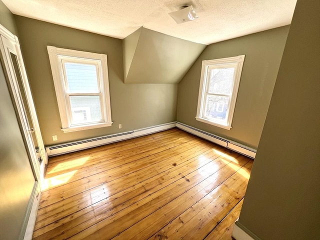 additional living space featuring wood-type flooring, baseboards, a textured ceiling, and a healthy amount of sunlight