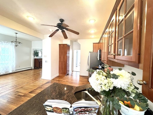 kitchen featuring brown cabinetry, a ceiling fan, wood finished floors, and glass insert cabinets