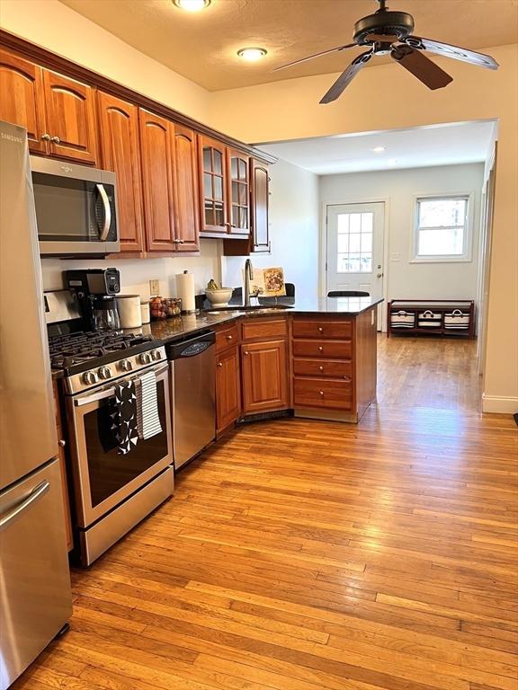 kitchen with dark countertops, brown cabinets, glass insert cabinets, a peninsula, and appliances with stainless steel finishes