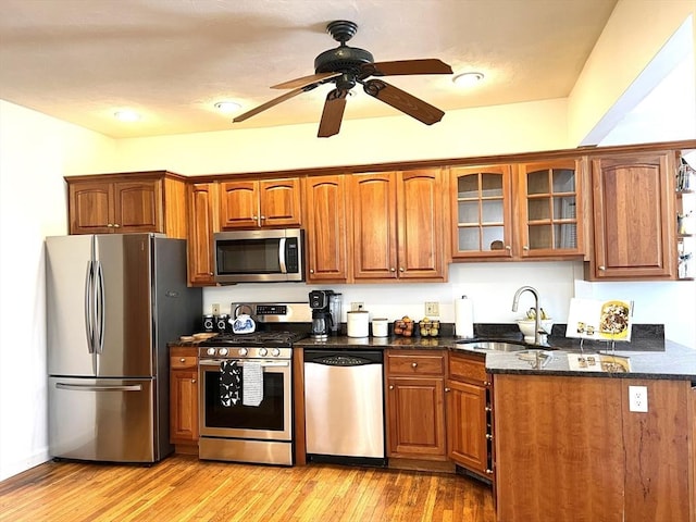 kitchen featuring a sink, glass insert cabinets, a ceiling fan, brown cabinetry, and appliances with stainless steel finishes