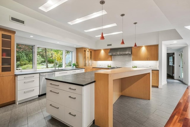 kitchen featuring white cabinetry, dishwasher, pendant lighting, wall chimney exhaust hood, and a center island