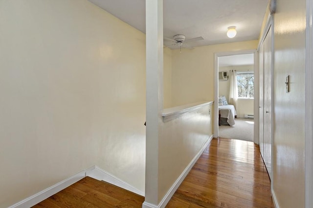 hall with baseboards, baseboard heating, wood finished floors, and a wall mounted AC