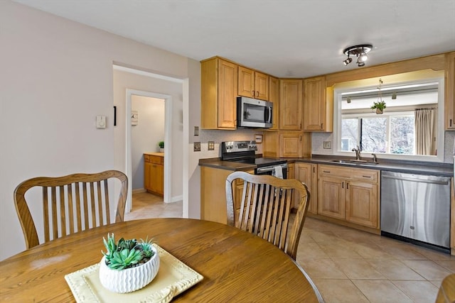 kitchen featuring decorative backsplash, dark countertops, a sink, appliances with stainless steel finishes, and light tile patterned floors
