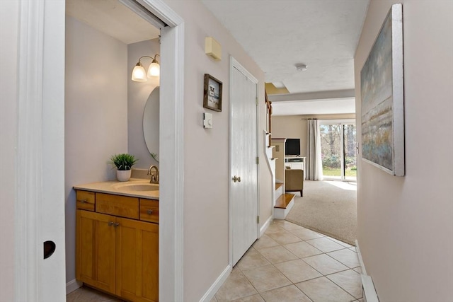 hall with a sink, baseboards, light tile patterned floors, and light carpet