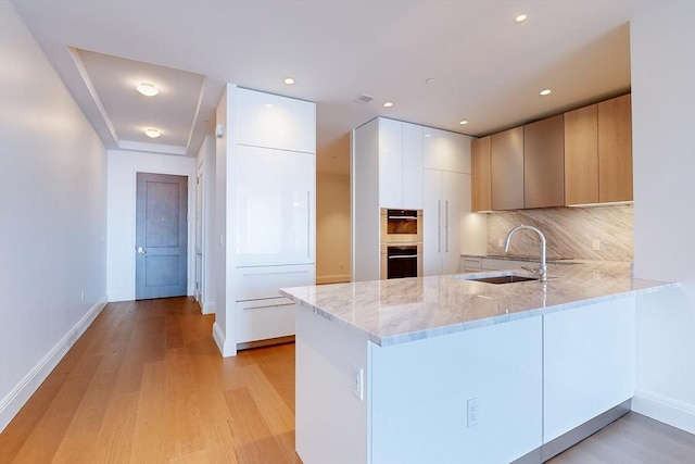 kitchen with light stone countertops, sink, light hardwood / wood-style flooring, backsplash, and kitchen peninsula