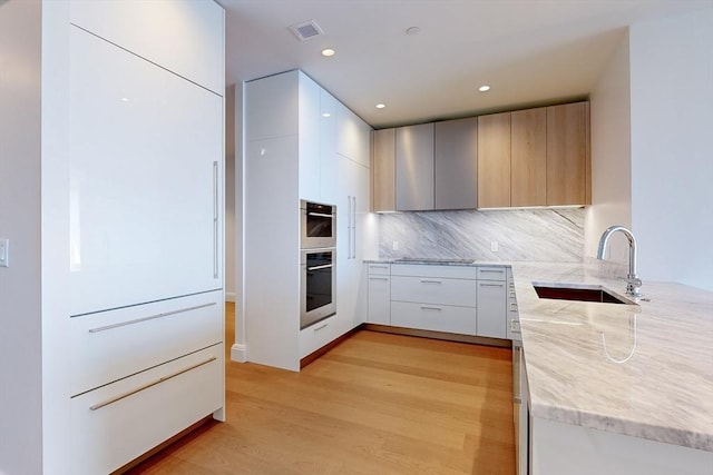 kitchen with sink, black electric cooktop, light wood-type flooring, tasteful backsplash, and white cabinetry