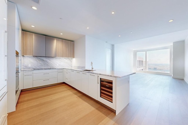 kitchen featuring kitchen peninsula, tasteful backsplash, light hardwood / wood-style flooring, white cabinets, and wine cooler