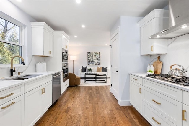 kitchen featuring appliances with stainless steel finishes, sink, white cabinets, and wall chimney exhaust hood