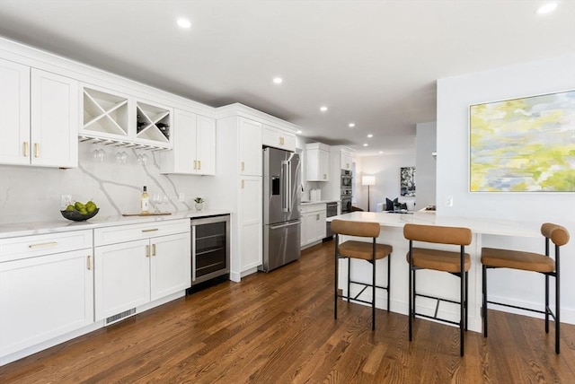 kitchen featuring a breakfast bar, white cabinets, dark hardwood / wood-style flooring, beverage cooler, and stainless steel appliances