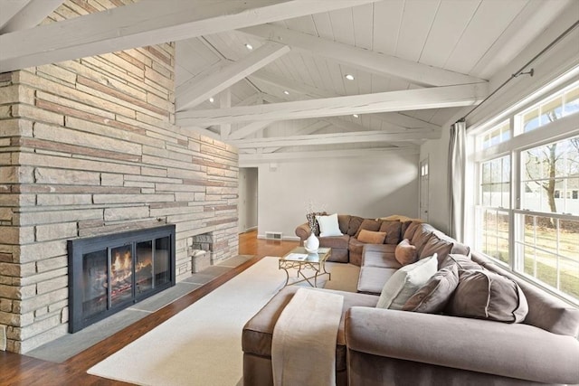 living area with lofted ceiling with beams, a stone fireplace, and a wealth of natural light