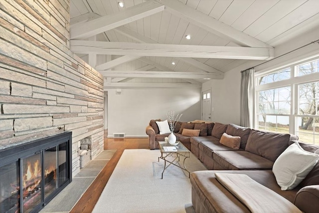 living area featuring visible vents, wood finished floors, a stone fireplace, wooden ceiling, and vaulted ceiling with beams