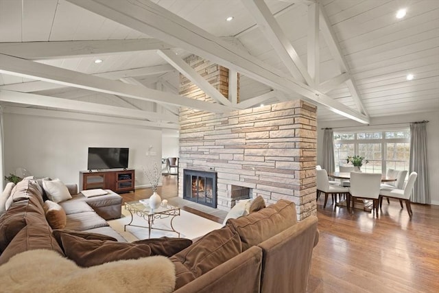 living room featuring wood finished floors, baseboards, vaulted ceiling with beams, recessed lighting, and a stone fireplace