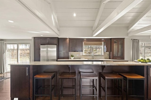 kitchen featuring beam ceiling, a sink, tasteful backsplash, stainless steel fridge, and dark brown cabinetry