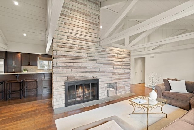 living area featuring a stone fireplace, lofted ceiling with beams, and wood finished floors