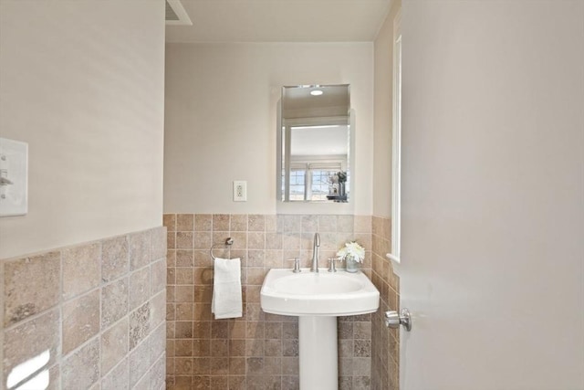 half bath featuring visible vents, tile walls, and a wainscoted wall