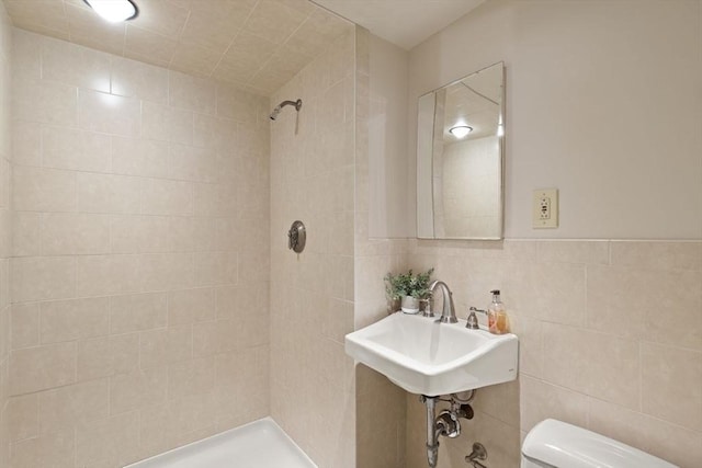 full bathroom with tile walls, toilet, a tile shower, and a sink