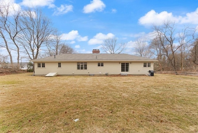 rear view of house with a lawn, a chimney, and fence