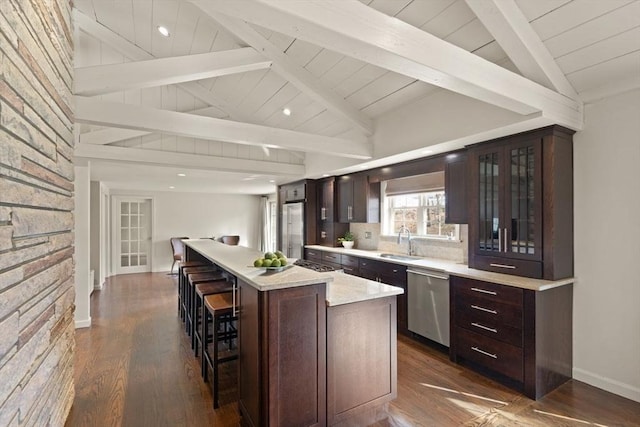 kitchen with a sink, dark brown cabinetry, appliances with stainless steel finishes, and vaulted ceiling with beams