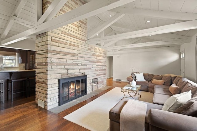 living area featuring visible vents, vaulted ceiling with beams, wood finished floors, and a fireplace