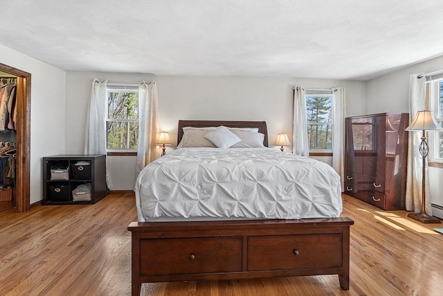 bedroom with wood finished floors, a walk in closet, a closet, and a baseboard radiator