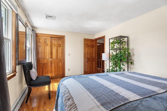 bedroom with baseboard heating, wood finished floors, and a closet
