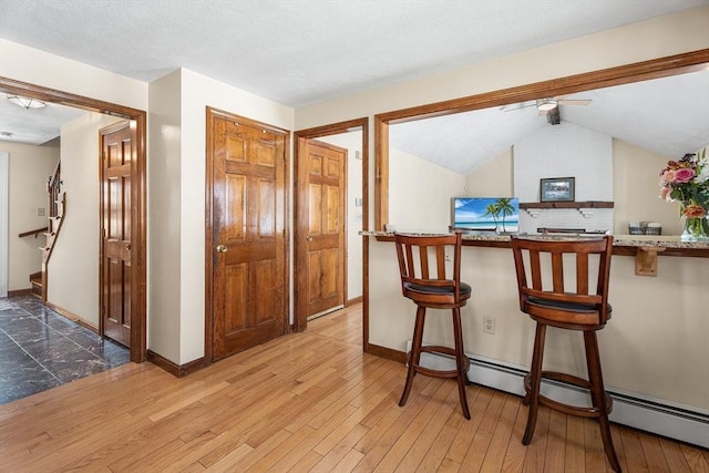 dining space with baseboards, light wood-type flooring, vaulted ceiling, and baseboard heating
