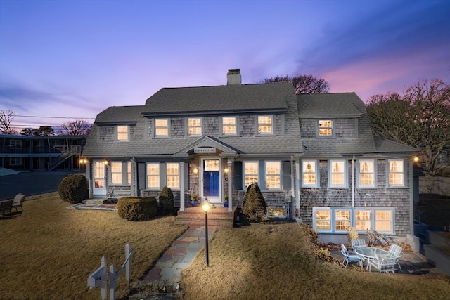 view of front of property featuring a lawn, a chimney, and a shingled roof