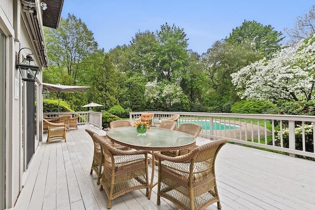 deck featuring outdoor dining area, view of scattered trees, and an outdoor pool