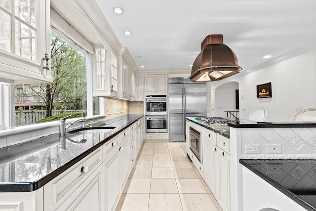 kitchen with built in appliances, a sink, tasteful backsplash, light tile patterned floors, and arched walkways