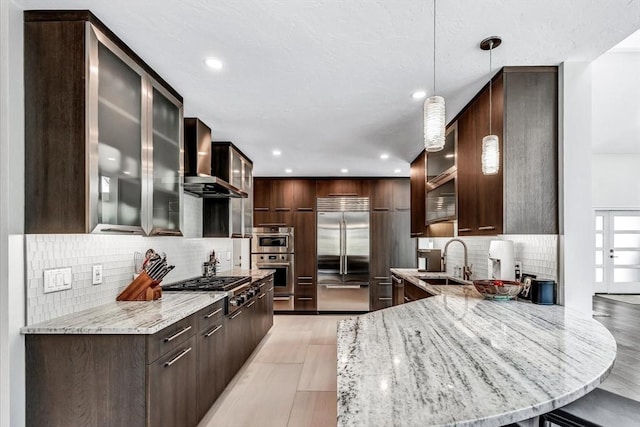 kitchen with dark brown cabinets, stainless steel built in fridge, gas stovetop, wall chimney exhaust hood, and a sink