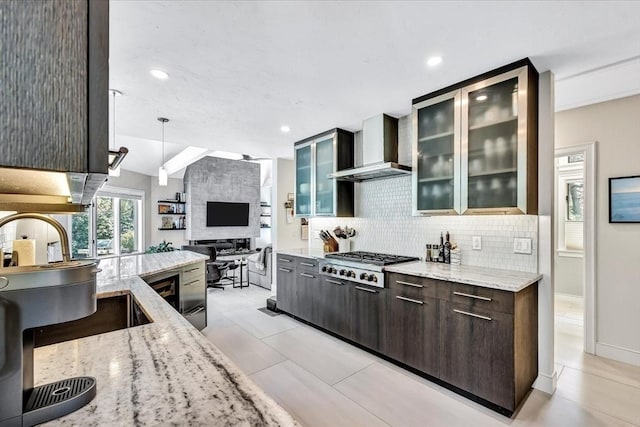 kitchen featuring backsplash, glass insert cabinets, light stone counters, stainless steel gas stovetop, and wall chimney exhaust hood