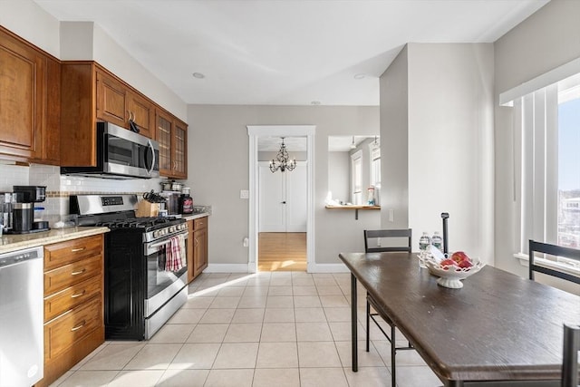 kitchen featuring appliances with stainless steel finishes, tasteful backsplash, light stone counters, light tile patterned floors, and a chandelier