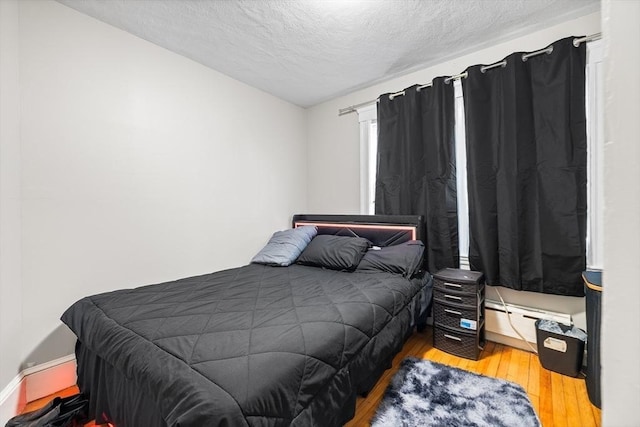 bedroom with hardwood / wood-style floors, a textured ceiling, and baseboard heating