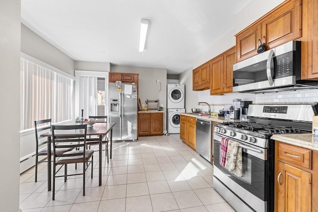 kitchen with stacked washer and clothes dryer, light stone countertops, light tile patterned floors, tasteful backsplash, and stainless steel appliances