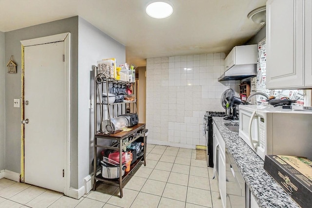 kitchen with stainless steel gas range oven, white cabinets, wall chimney exhaust hood, light tile patterned floors, and light stone counters