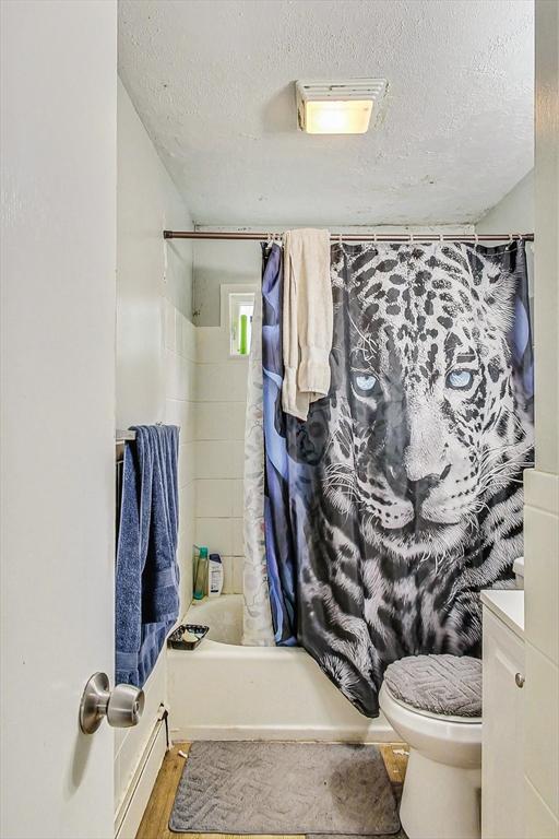 full bathroom with vanity, a textured ceiling, shower / bath combo with shower curtain, hardwood / wood-style floors, and toilet