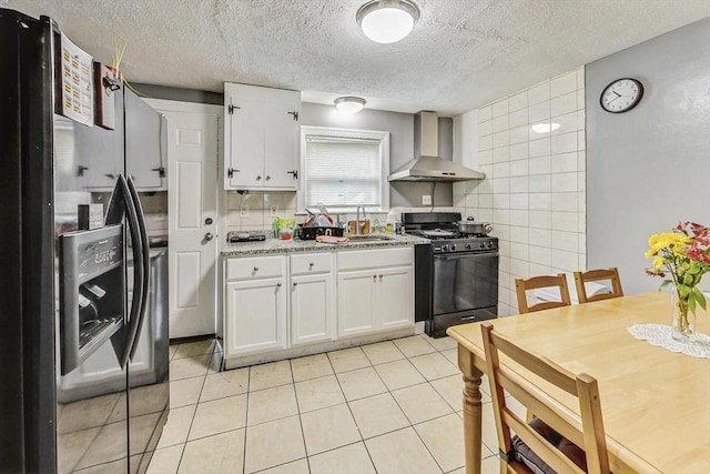 kitchen featuring light tile patterned flooring, stainless steel refrigerator with ice dispenser, wall chimney exhaust hood, gas stove, and white cabinetry