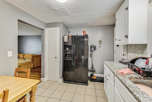 kitchen featuring light stone countertops, a textured ceiling, light tile patterned floors, black fridge with ice dispenser, and white cabinetry