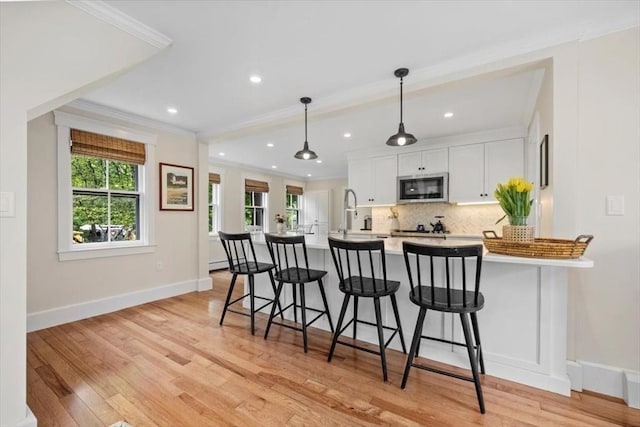 22 High St, Hingham, MA 02043 - kitchen featuring stainless steel microwave, a kitchen bar, ornamental molding, white cabinetry, and light countertops