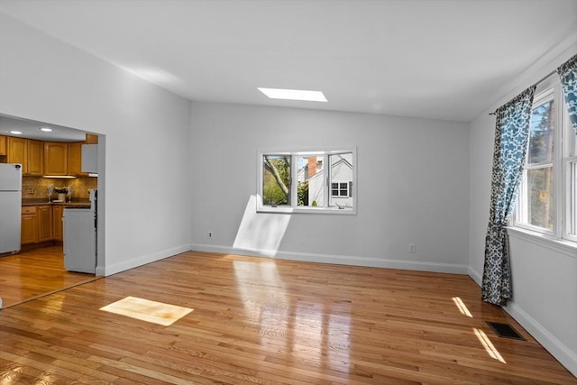 unfurnished living room with baseboards, visible vents, lofted ceiling with skylight, and light wood finished floors