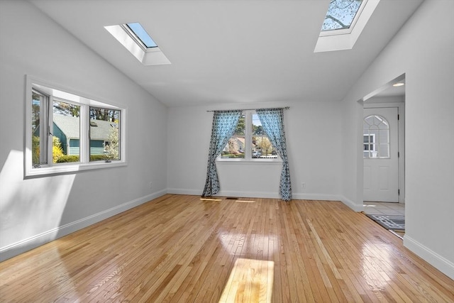 spare room featuring baseboards, light wood finished floors, and vaulted ceiling with skylight