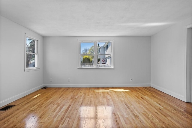 spare room featuring a healthy amount of sunlight, baseboards, light wood finished floors, and visible vents