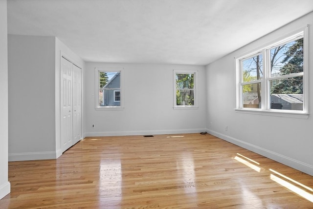 spare room with baseboards, light wood-style flooring, and a wealth of natural light