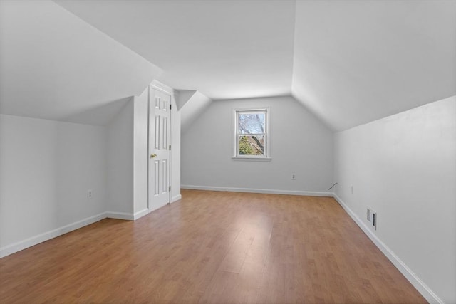 additional living space with baseboards, visible vents, light wood finished floors, and lofted ceiling