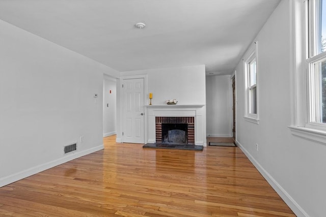 unfurnished living room with a healthy amount of sunlight, a fireplace, light wood-type flooring, and visible vents