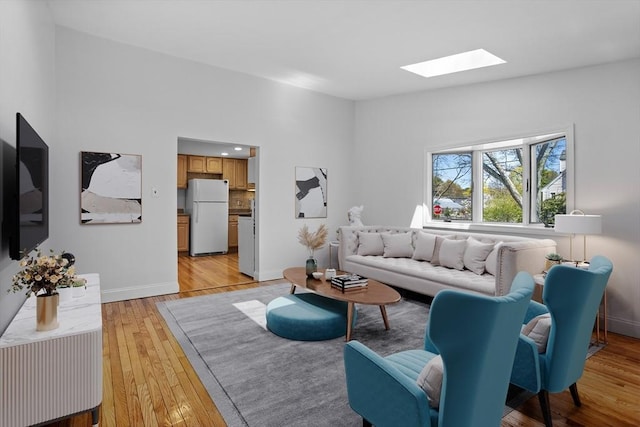 living area with a skylight, baseboards, and light wood finished floors