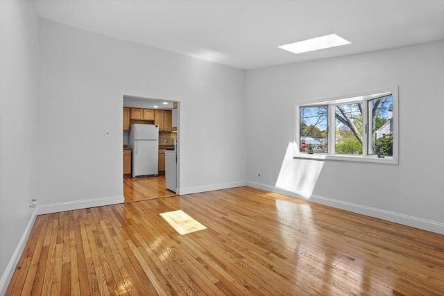 unfurnished living room with light wood-type flooring, baseboards, and a skylight