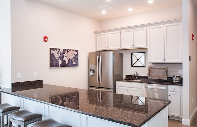 kitchen with white cabinetry, sink, kitchen peninsula, appliances with stainless steel finishes, and dark stone countertops