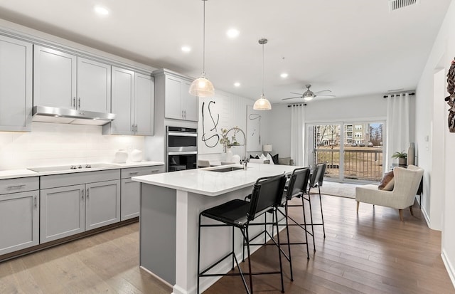 kitchen with a center island with sink, sink, gray cabinetry, and double oven